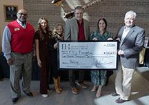 Several people pose with an oversized donation "check" for $100,000.